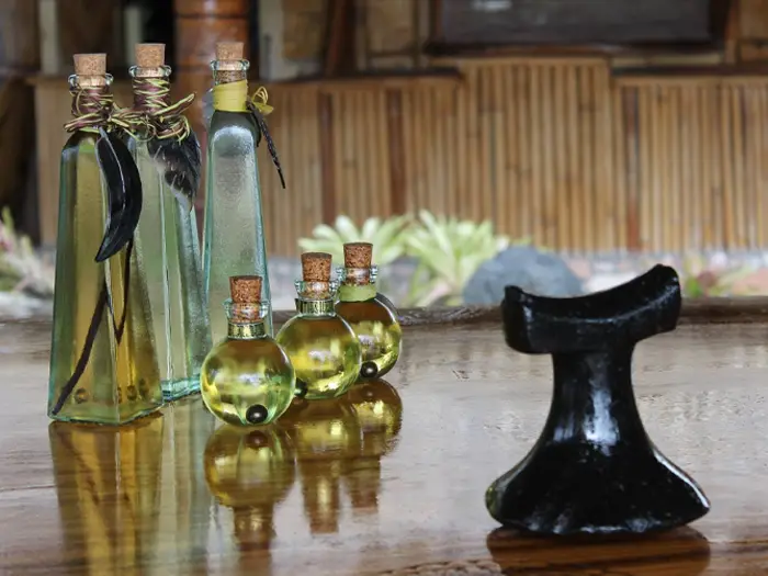 Monoi de Tahiti: Origin, How It’s Made, and How to Identify Authentic Monoi de Tahiti 3 Monoi oil and a Polynesian tool placed on a table, with tiare flowers in the distance